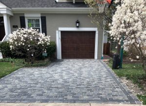 Brick paver driveway cost Chicago suburbs – Pavestone Brick Paving Brick paver driveway in front of a Chicago-area home with a wood garage door and blooming magnolia