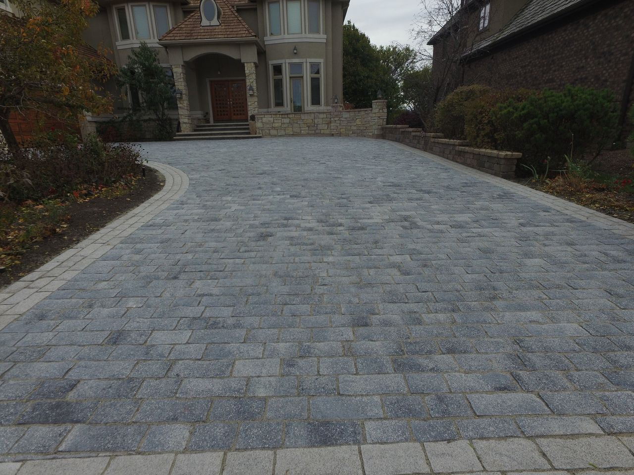Long cobblestone-style brick paver driveway with a contrasting border leading to a Chicago-area home