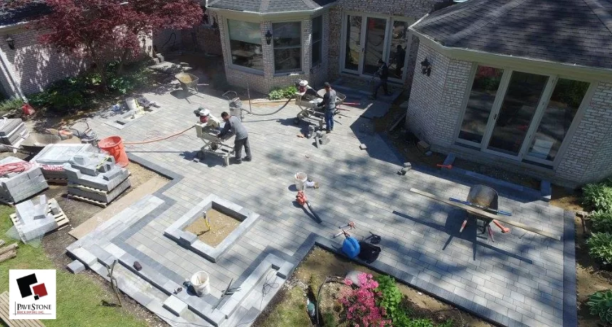 Crew installing a paver patio with cutting equipment and stacked pavers behind a brick home in the Chicago suburbs